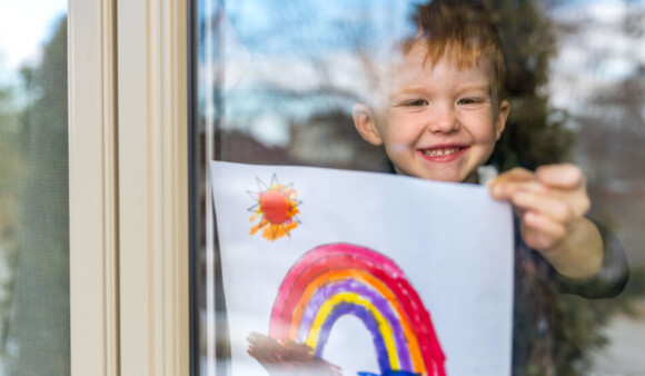 Child smiling and taping a picture of a rainbow to a window