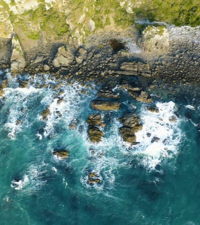 A top-down aerial view of waves crashing against a rocky shoreline