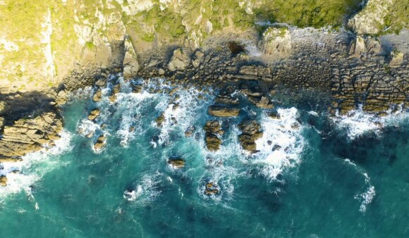 A top-down aerial view of waves crashing against a rocky shoreline